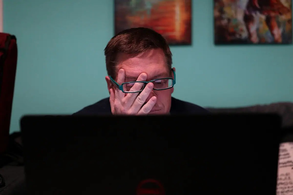 A tired man rubbing his eyes in front of a laptop