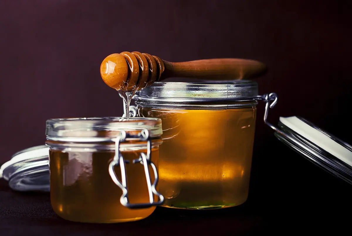Two glass jars of golden honey with a wooden honey dipper