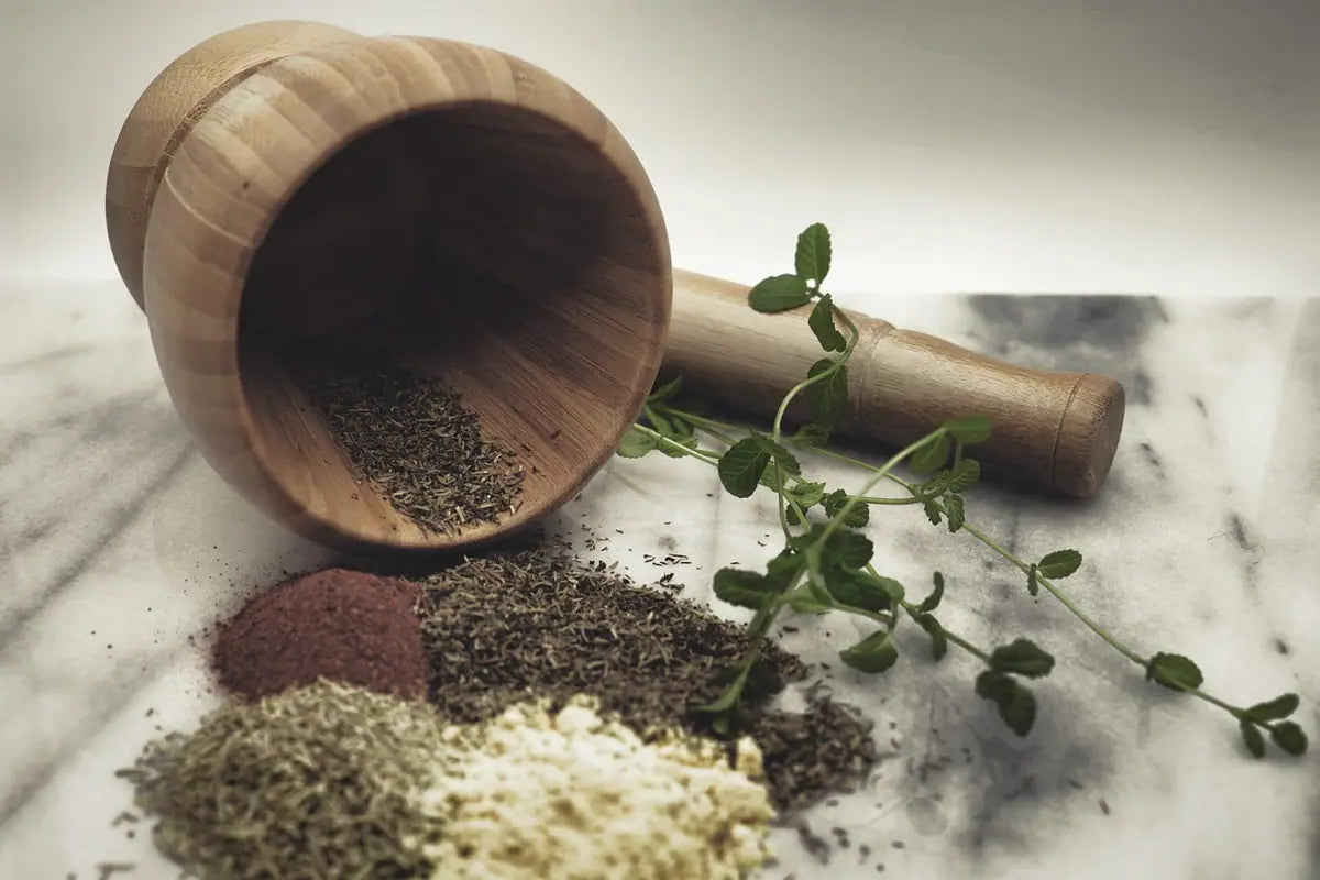 A wooden mortar and pestle with ground herbs, seeds and spices